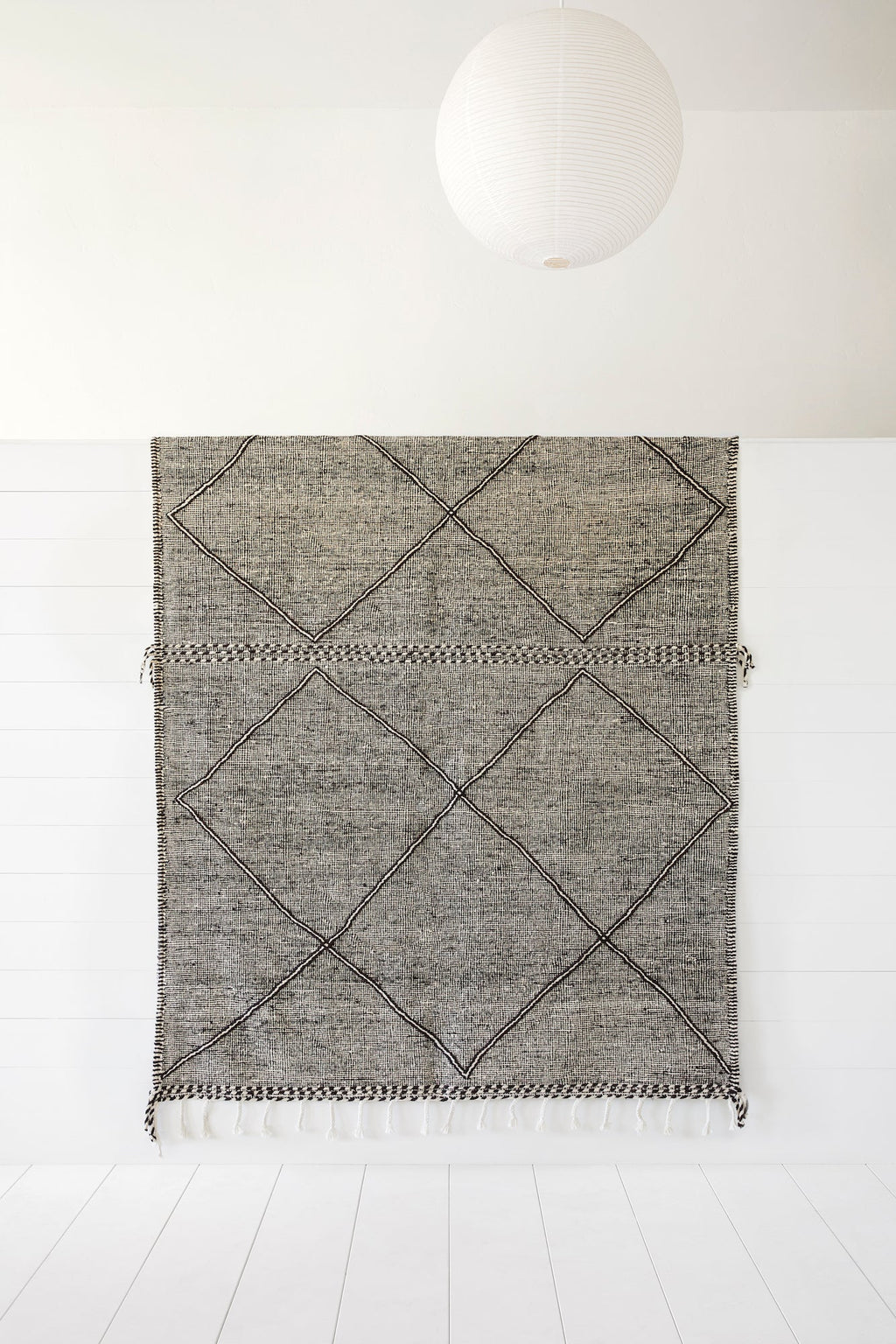 Moroccan flat weave Kilim rug with geometric diamond pattern and fringe, 6'-10" x 10'-3" displayed on white wall under paper lantern