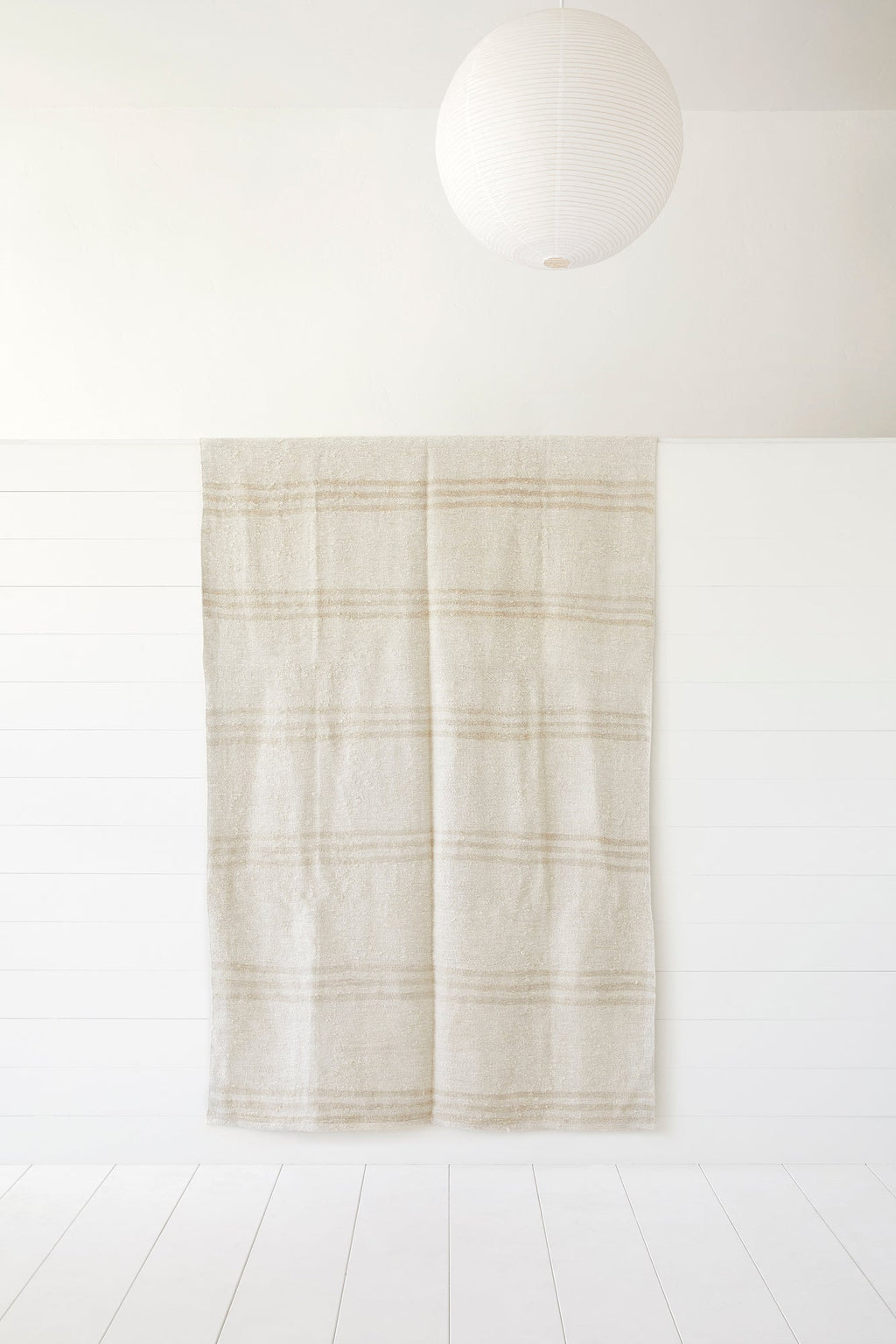 Neutral beige and cream Turkish Kilim rug with tribal stripes hanging on white wall under paper lantern light