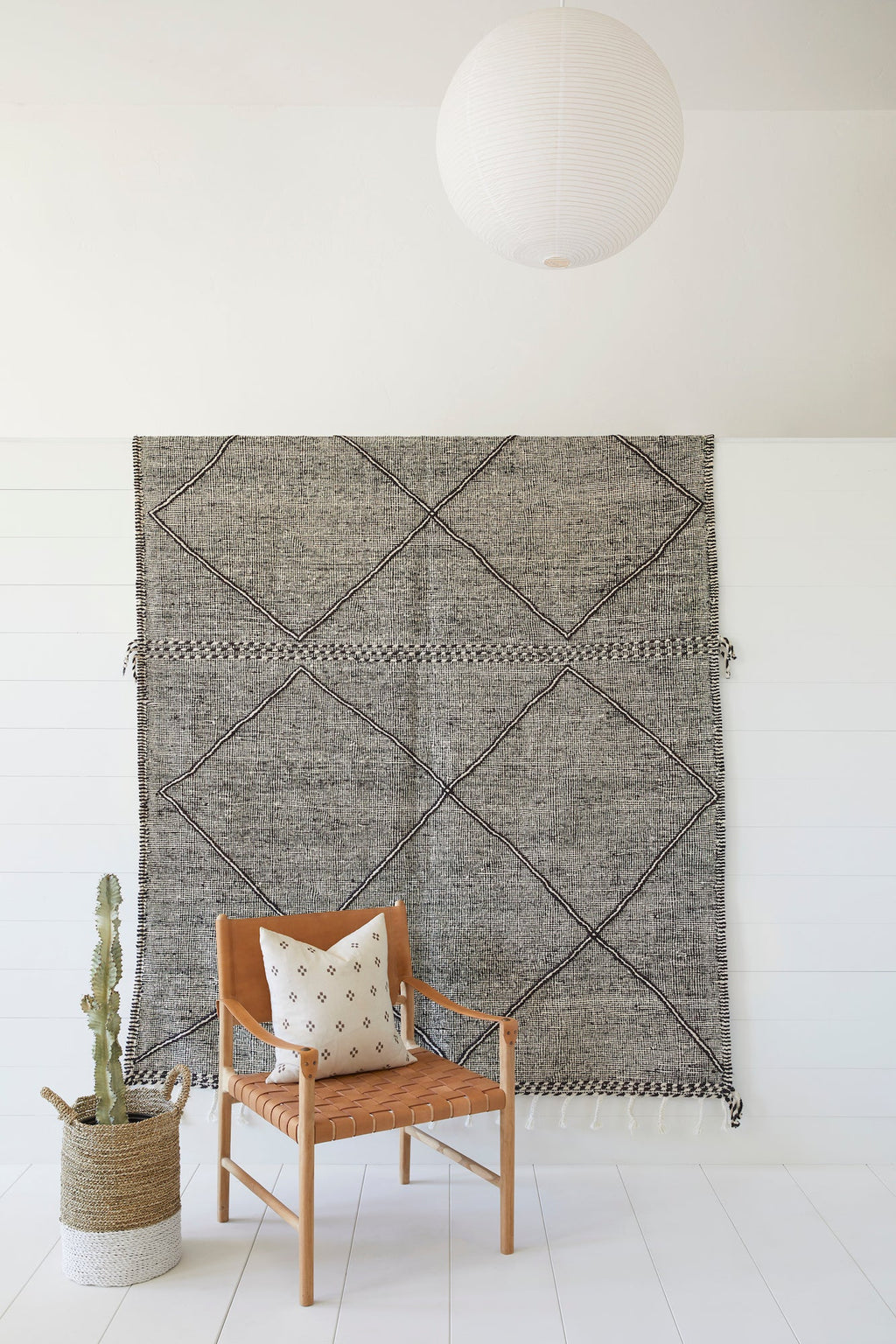 Moroccan Flat Weave Kilim Rug with geometric diamond pattern hanging on white wall above wooden chair and potted cactus