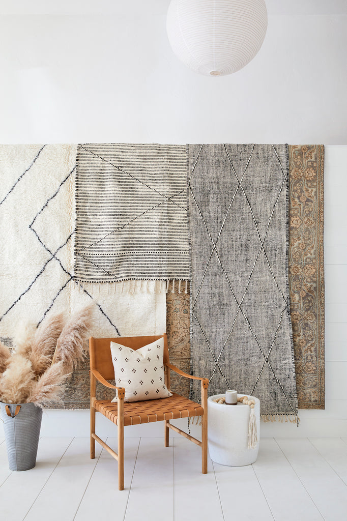 Styled view of No. 40 - Moroccan Flat Weave Kilim Rug layered with additional rugs and staged along side of a Leather Strap Safari Lounge Chair against a white background. - Saffron and Poe