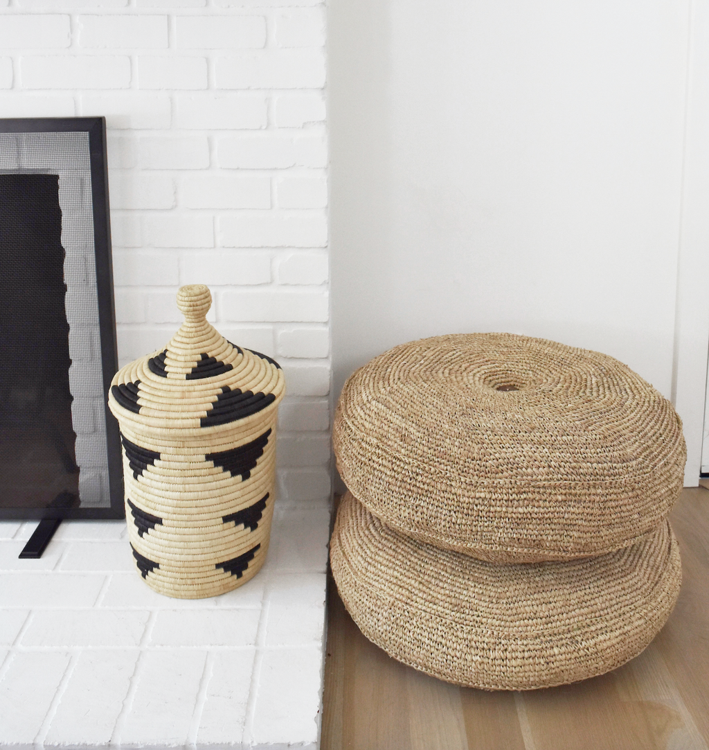 Natural woven hyacinth poufs stacked next to woven basket by white brick fireplace