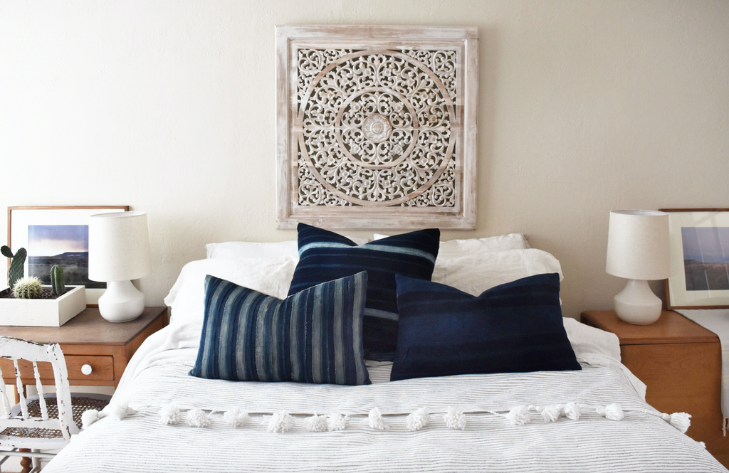 Light grey and white striped Moroccan Pom Bed Throw with tassels on a bed with blue pillows in a bohemian bedroom