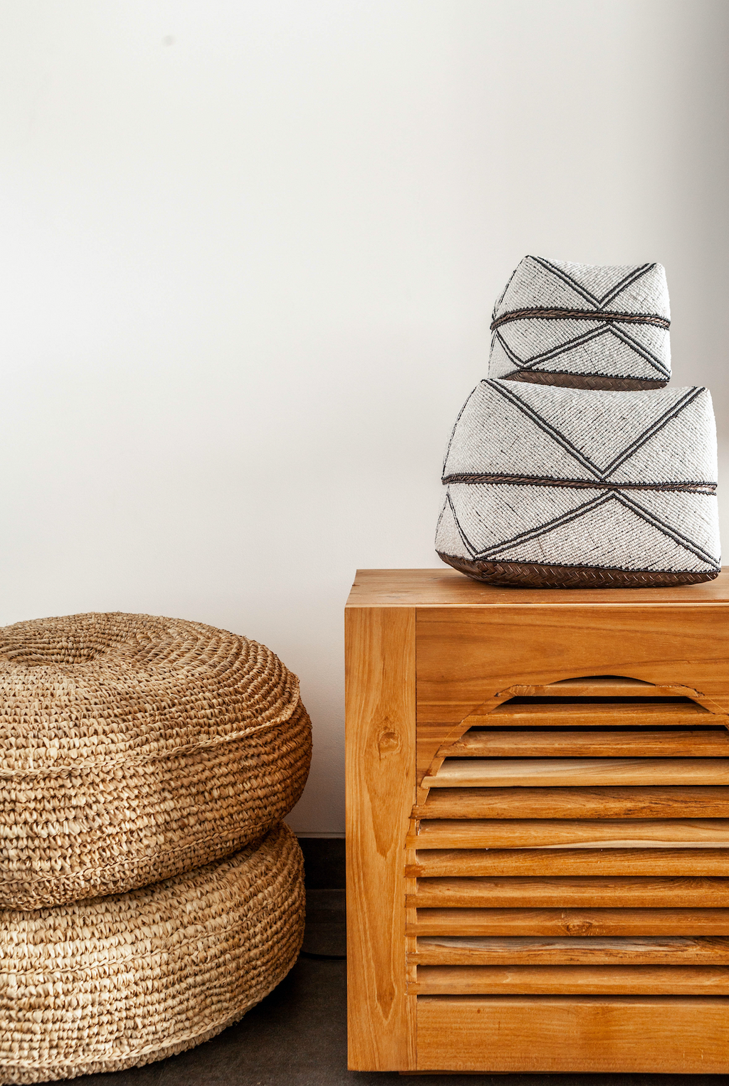 Natural woven hyacinth poufs stacked beside wooden cabinet in minimalist room