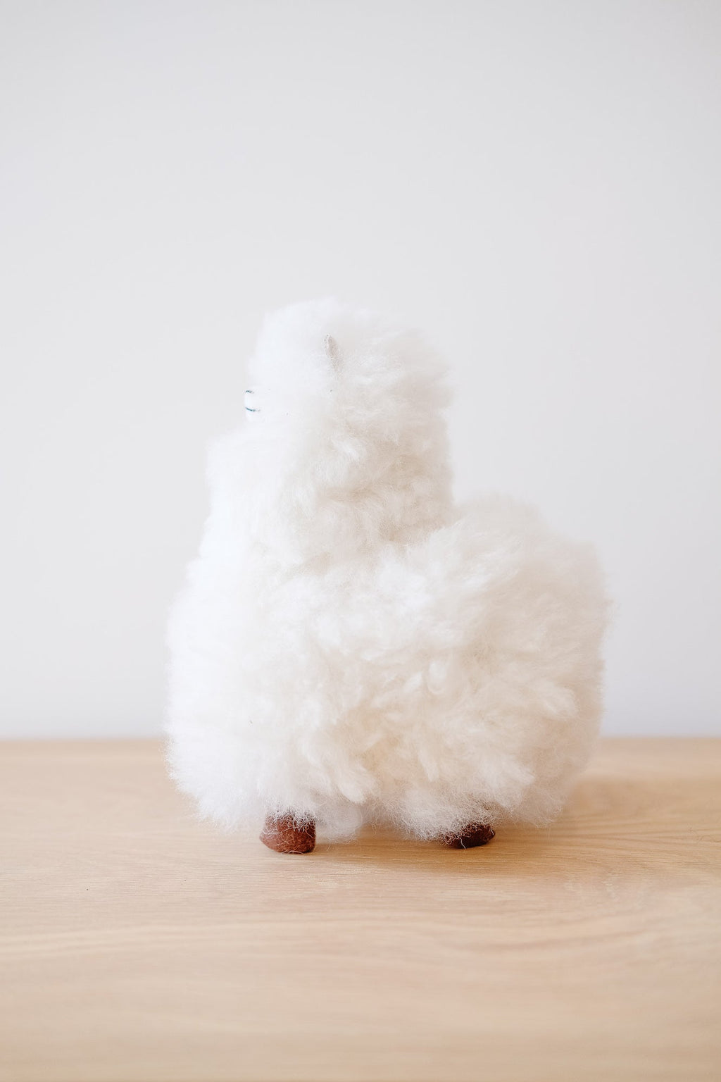White fluffy Alpaquita stuffed animal made from 100% baby alpaca wool on wooden surface