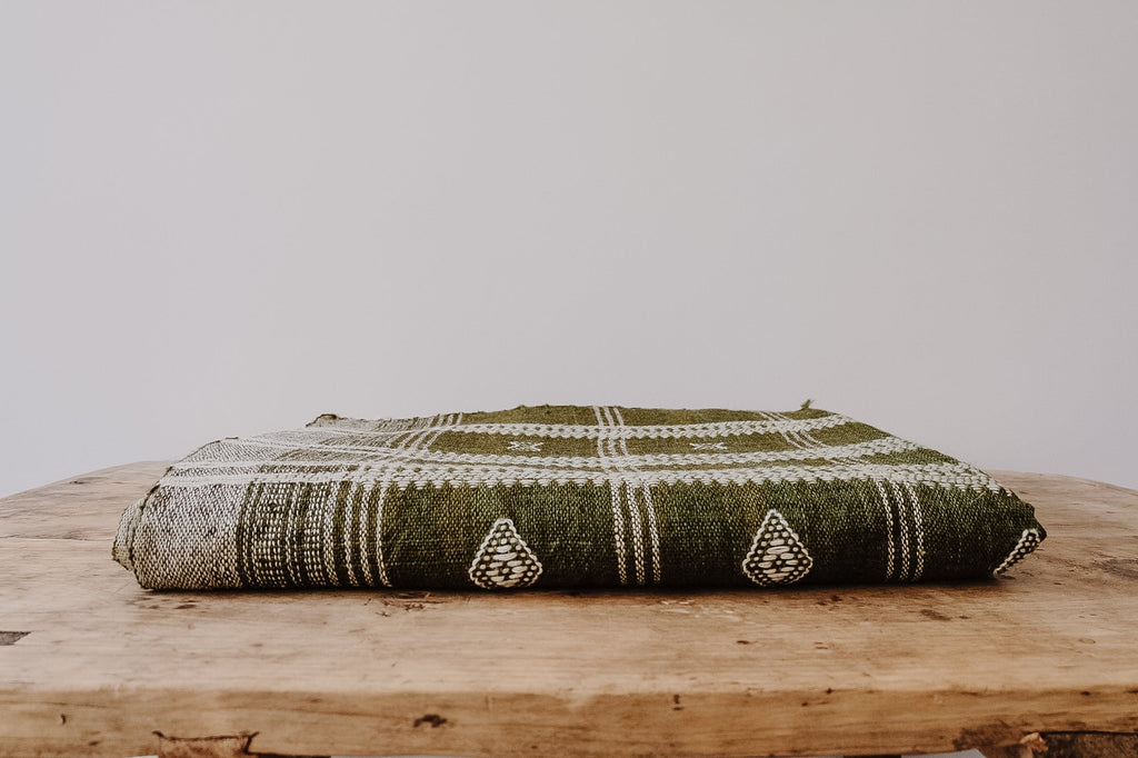 Handwoven Bhujodi Blanket in olive with pastoral motifs folded on wooden surface