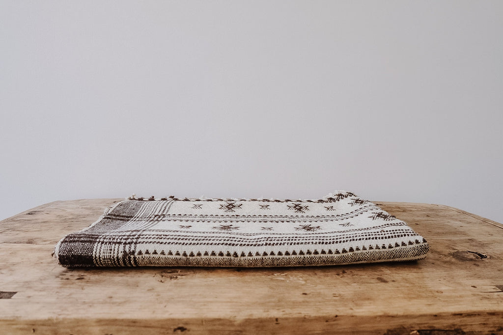 Handwoven Bhujodi bed throw with natural wool and traditional Indian motifs folded on wooden table