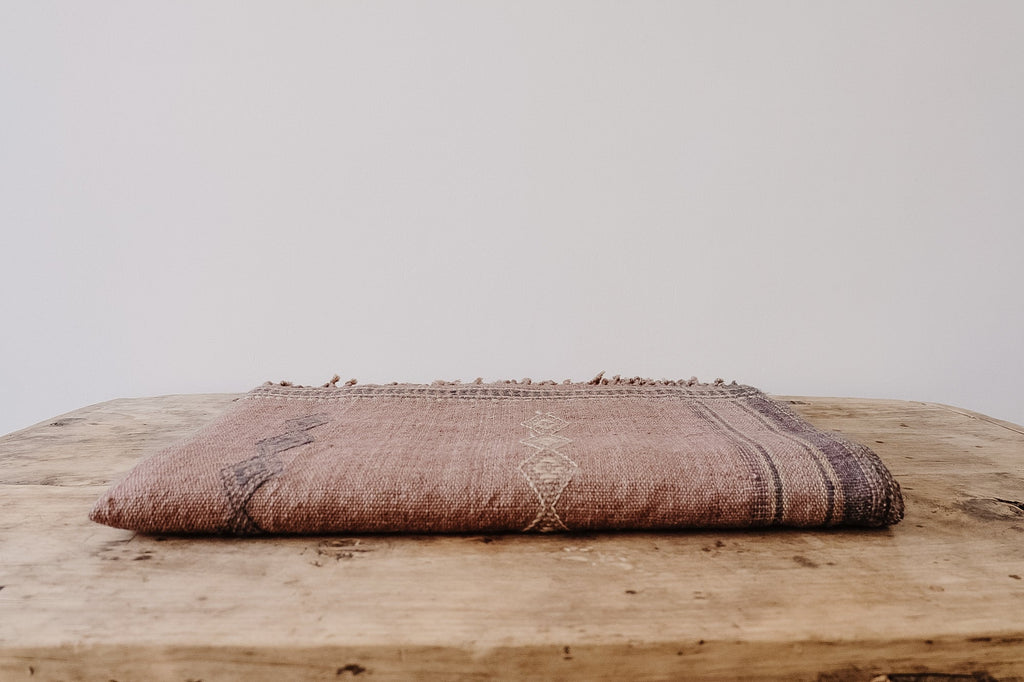 Handwoven Bhujodi bed throw in rust color folded on wooden surface showcasing intricate traditional Indian textile design