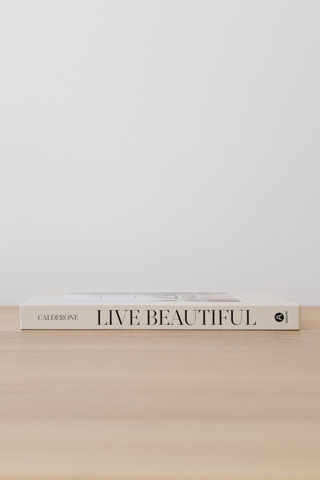 Live Beautiful design book by Athena Calderone on wooden surface against white background