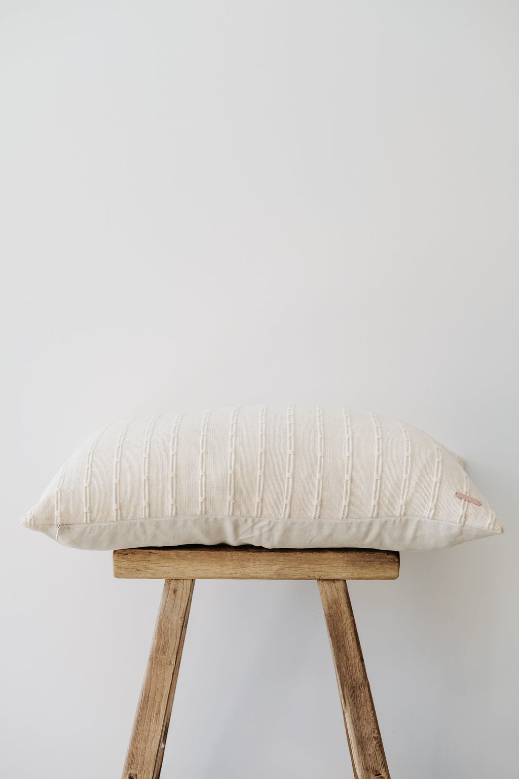 Ivory embroidered pillow with subtle textured pattern on wooden stool against white background