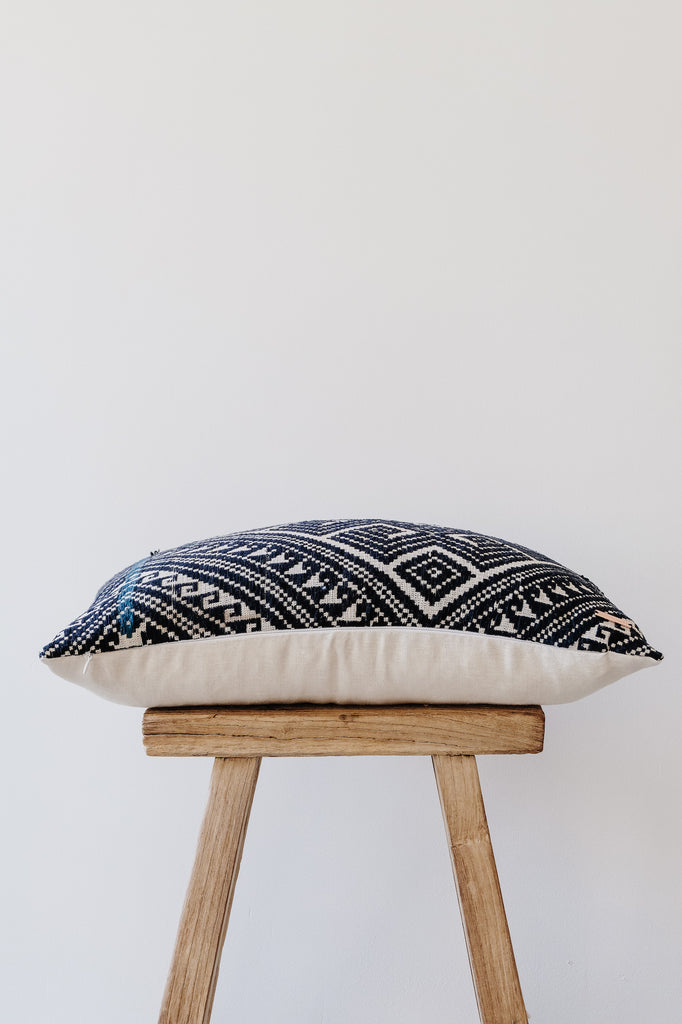 Side view of No. 20 - Antique Miao Lumbar Pillow on an Antique Stool against a white wall. - Saffron and Poe