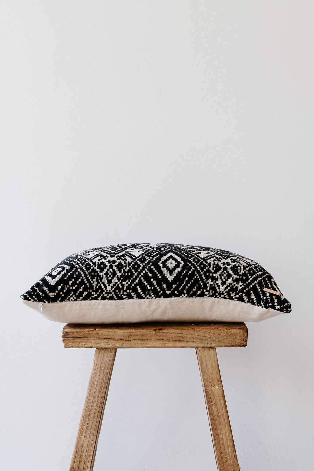 Antique Miao lumbar pillow with black and white traditional woven patterns on a wooden stool against a plain background