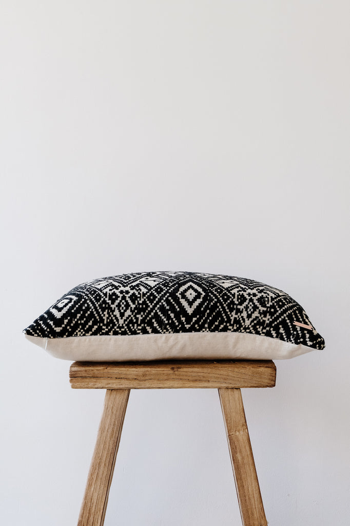 Side view of No. 22 - Antique Miao Lumbar Pillow on an Antique Stool against a white wall. - Saffron and Poe