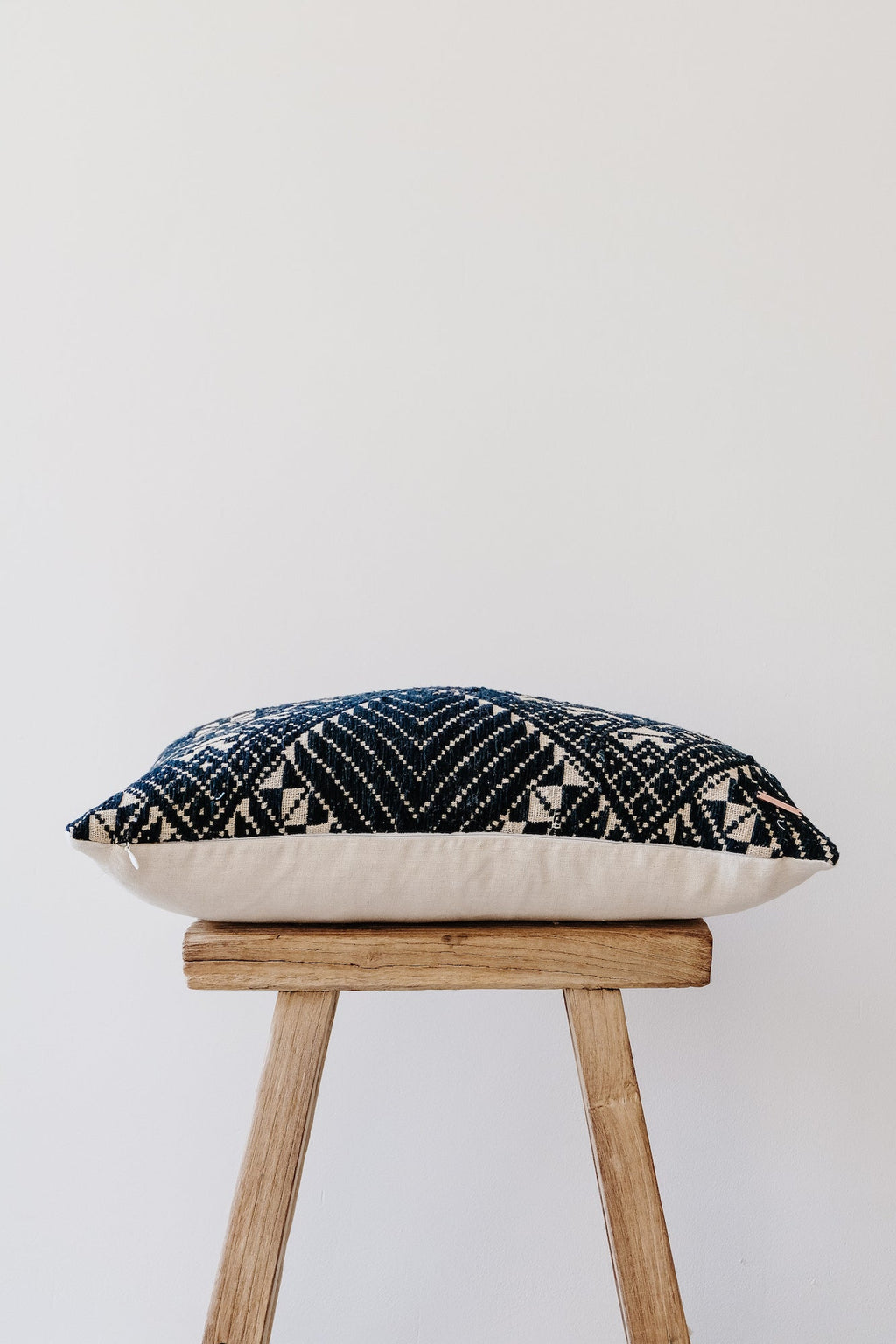 Antique Miao lumbar pillow with black and white geometric embroidery on wooden stool against white background
