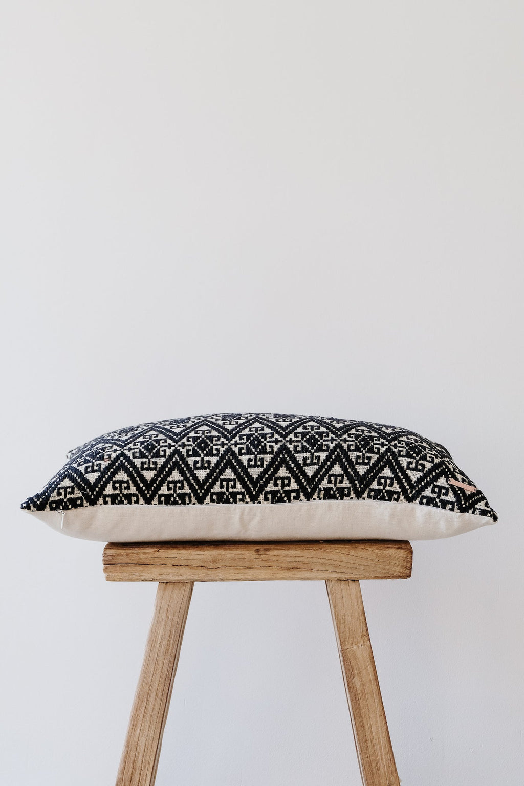 Antique Miao lumbar pillow with traditional black and white geometric embroidery on wooden stool against white background