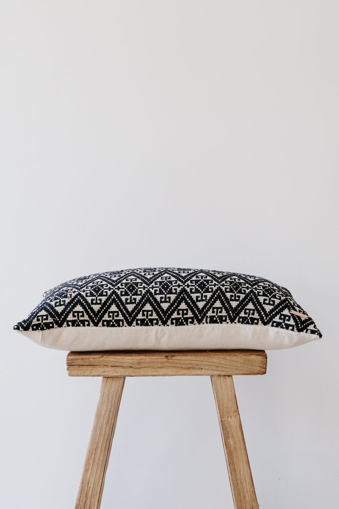 Side view of No. 24 - Antique Miao Lumbar Pillow on an Antique Stool against a white wall. - Saffron and Poe
