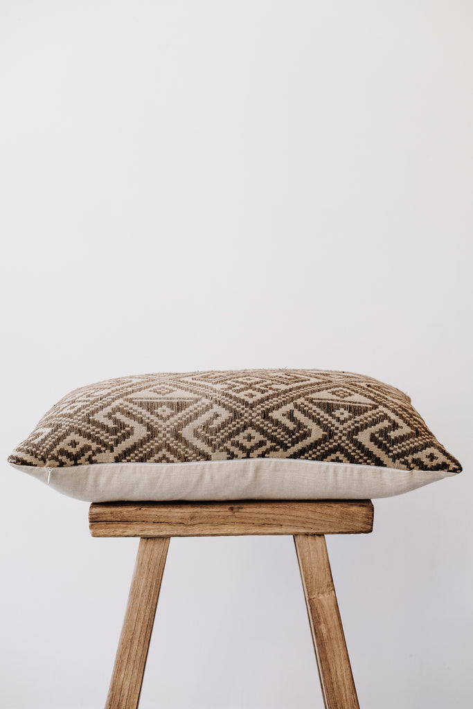 Side view of No. 25 - Antique Miao Lumbar Pillow on an Antique Stool against a white wall. - Saffron and Poe