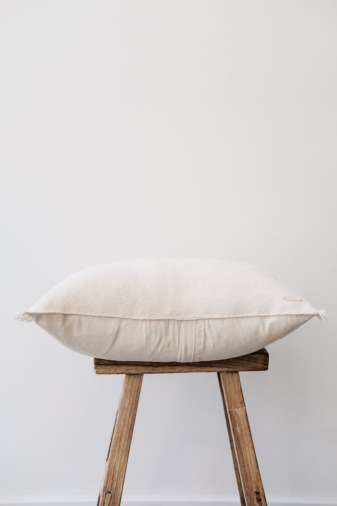 Side view of No. 28 - Baby Alpaca Pillow - Ivory on an Antique Stool against a white wall. - Saffron and Poe