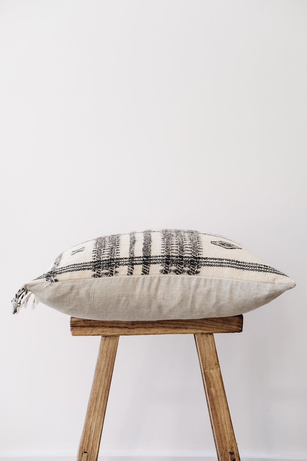Handwoven Bhujodi Pillow with black and white pastoral motifs on wooden stool against white background