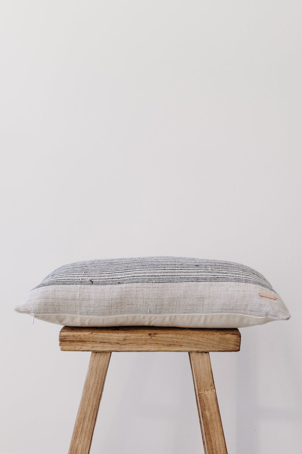 Vintage Hmong lumbar pillow with indigo stripes and linen backing on wooden stool