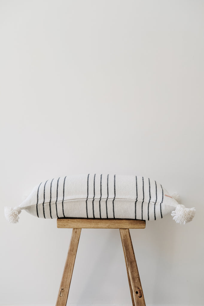 Side view of No. 42 - Moroccan Pom Pom Striped Pillow - Black on a Chinese Stool against a white wall. - Saffron and Poe
