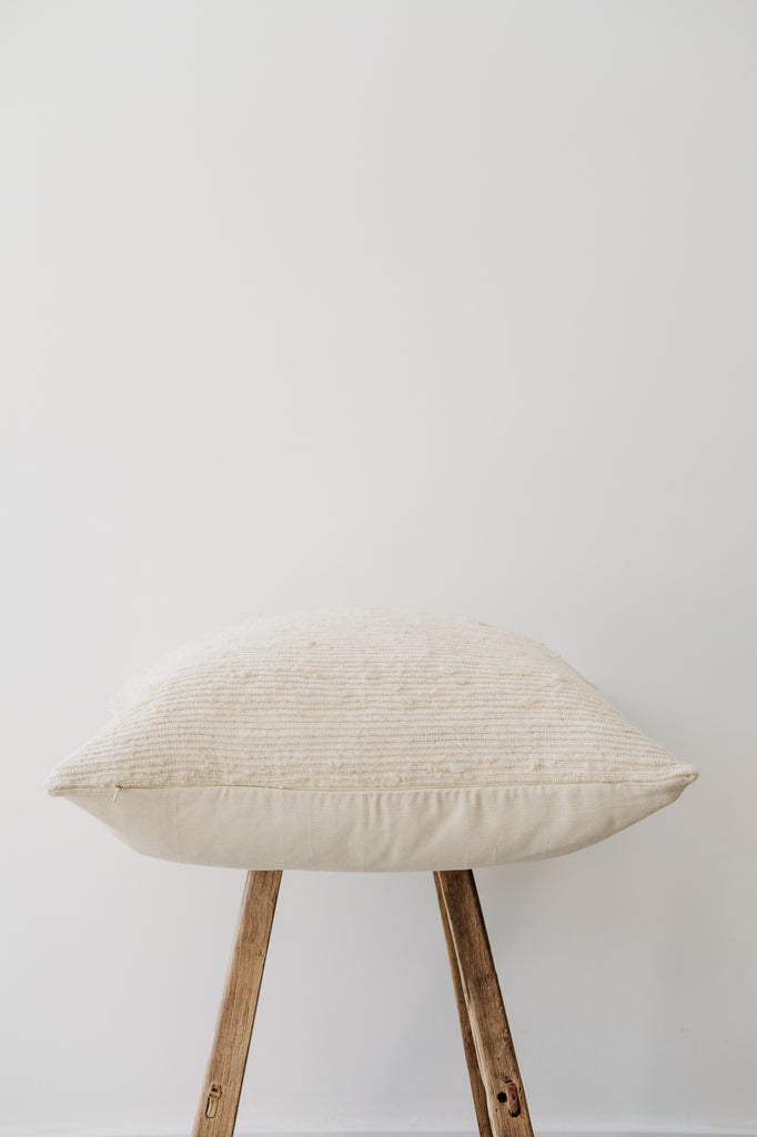 Side view of No. 47 - Ivory Handwoven Columbian Pillow on a Chinese Stool against a white wall. - Saffron and Poe