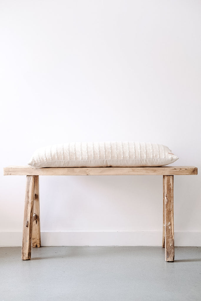Side view of No. 11 - Hmong Hemp Lumbar Pillow - Extra Long on an Antique Bench against a white wall. - Saffron and Poe