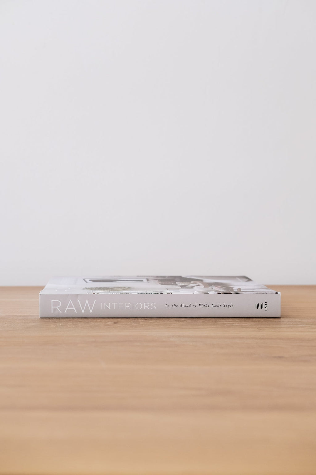 Book titled Raw Interiors about Wabi-Sabi style placed on wooden surface with white background