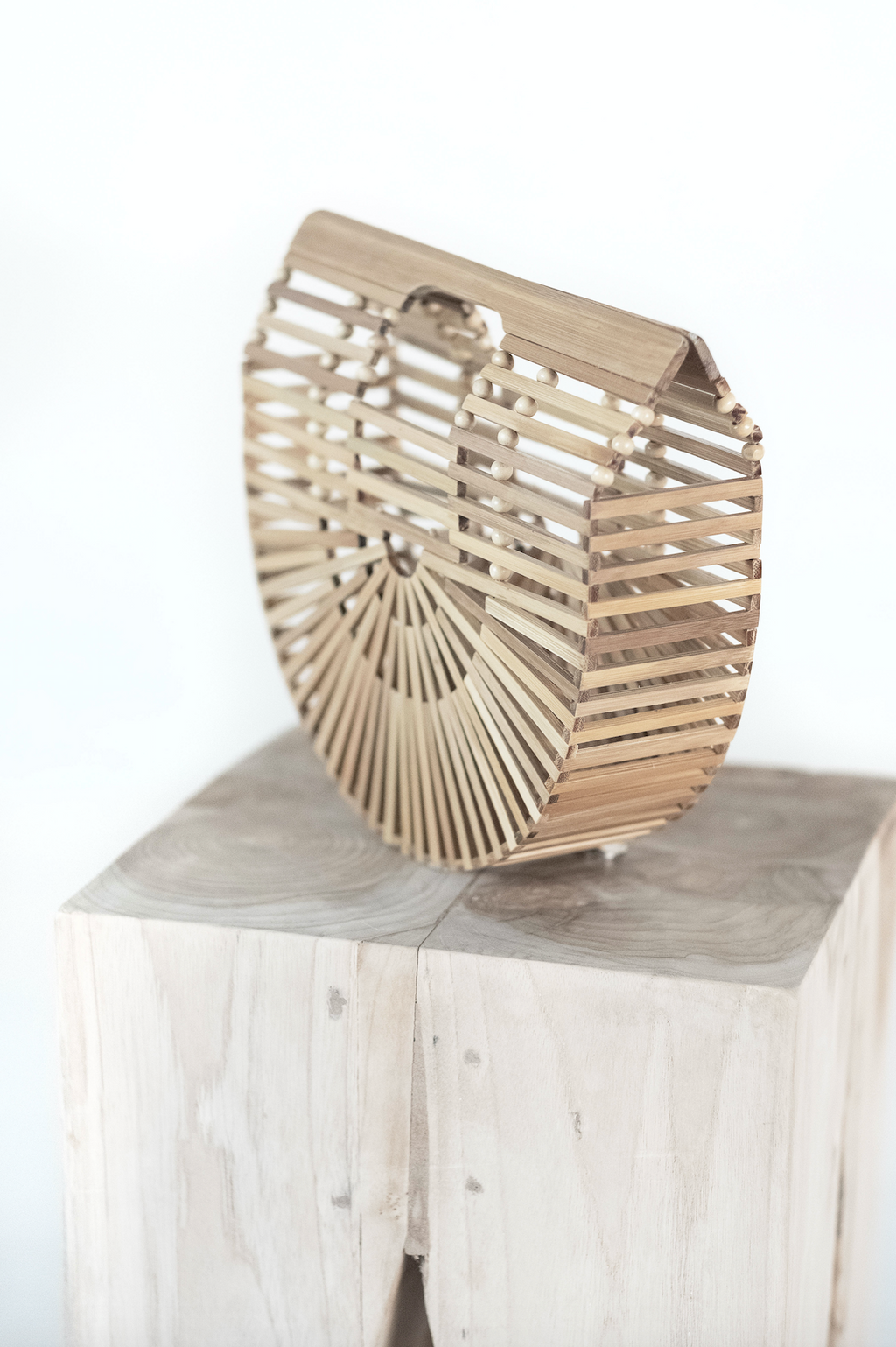 Handcrafted bamboo crescent clutch with geometric pattern on wooden block