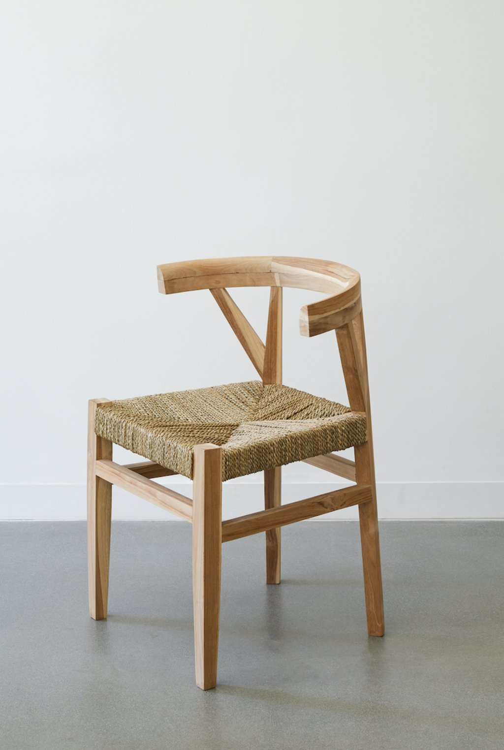 Woven wishbone dining chair with braided rattan seat and curved teak frame on gray floor
