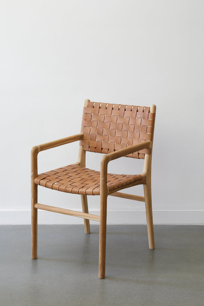 Angled side view of the Woven Leather Strap Dining Arm Chair in Beige against a white background and concrete floors. - Saffron and Poe