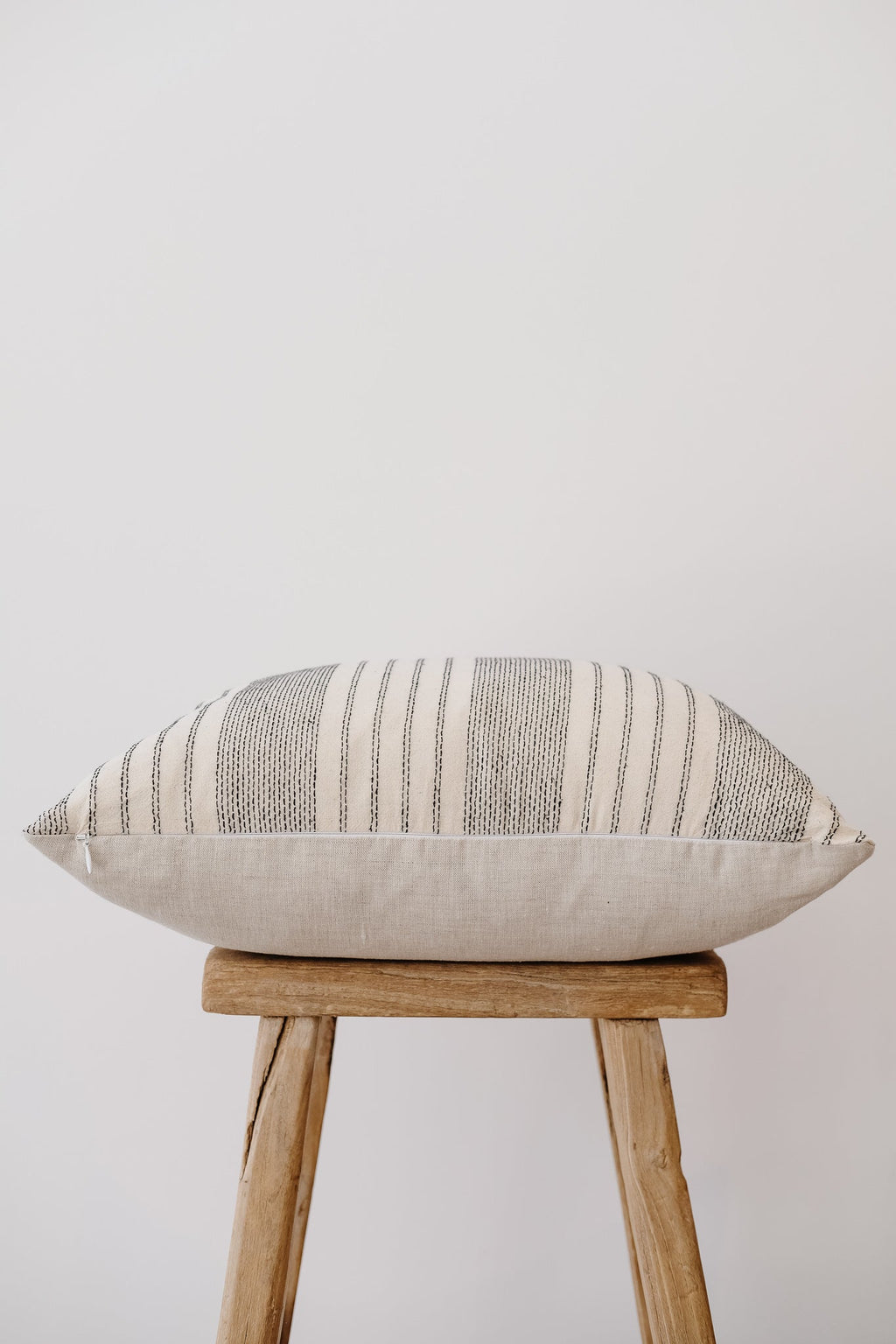 Ivory embroidered pillow with neutral textured pattern on wooden stool against white background
