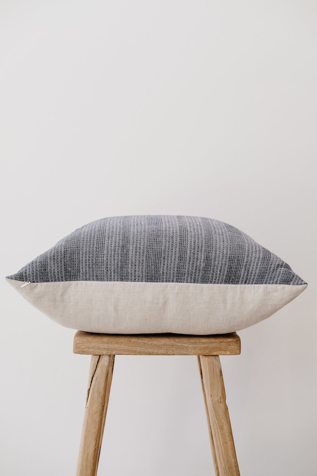 Dusty blue embroidered pillow with neutral textured pattern on wooden stool