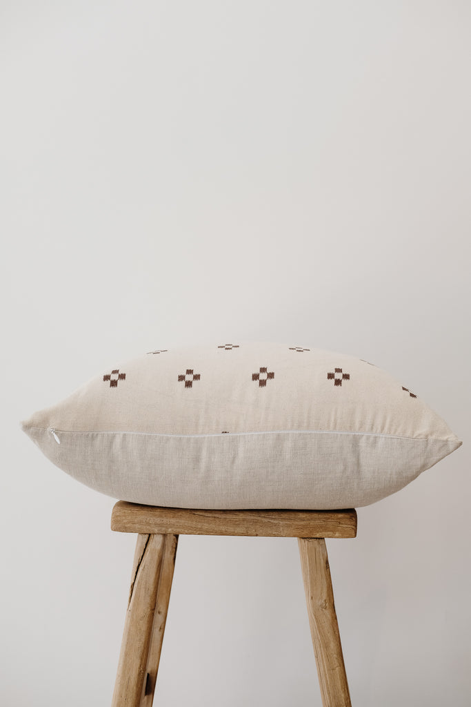 Side view of No. 16 - Hmong Hemp Batik Pillow on an Antique Stool against a white wall. - Saffron and Poe