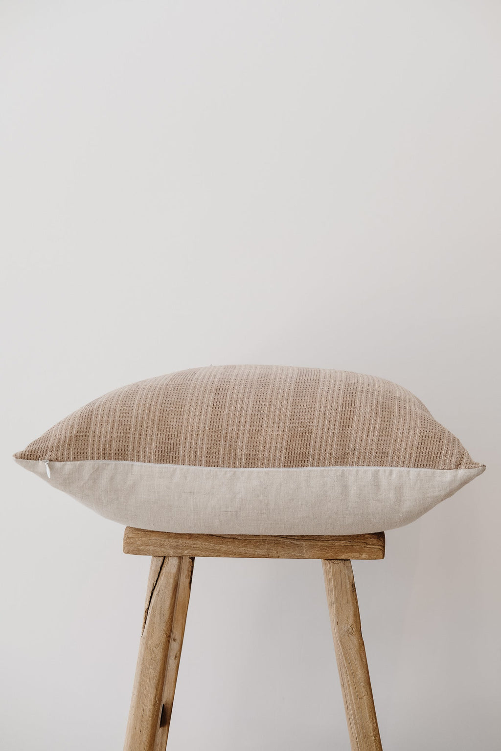 Beige embroidered pillow with textured pattern on wooden stool against white background