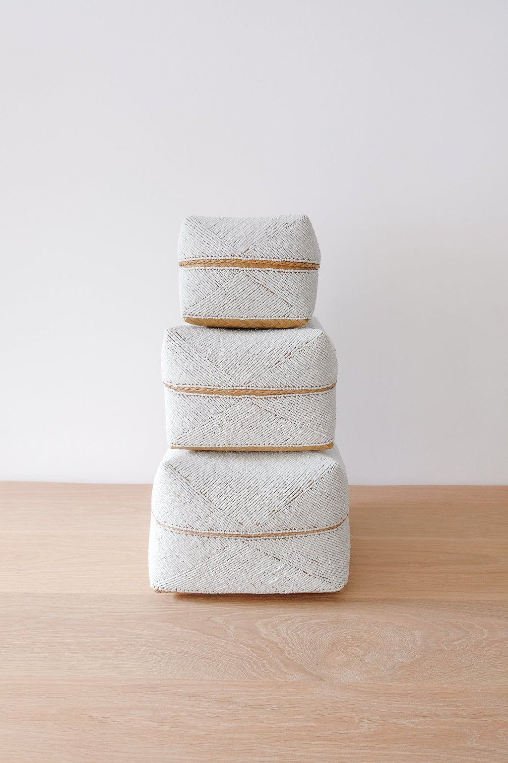 Stacked hand-beaded Bali baskets in solid white with woven bamboo on wooden surface