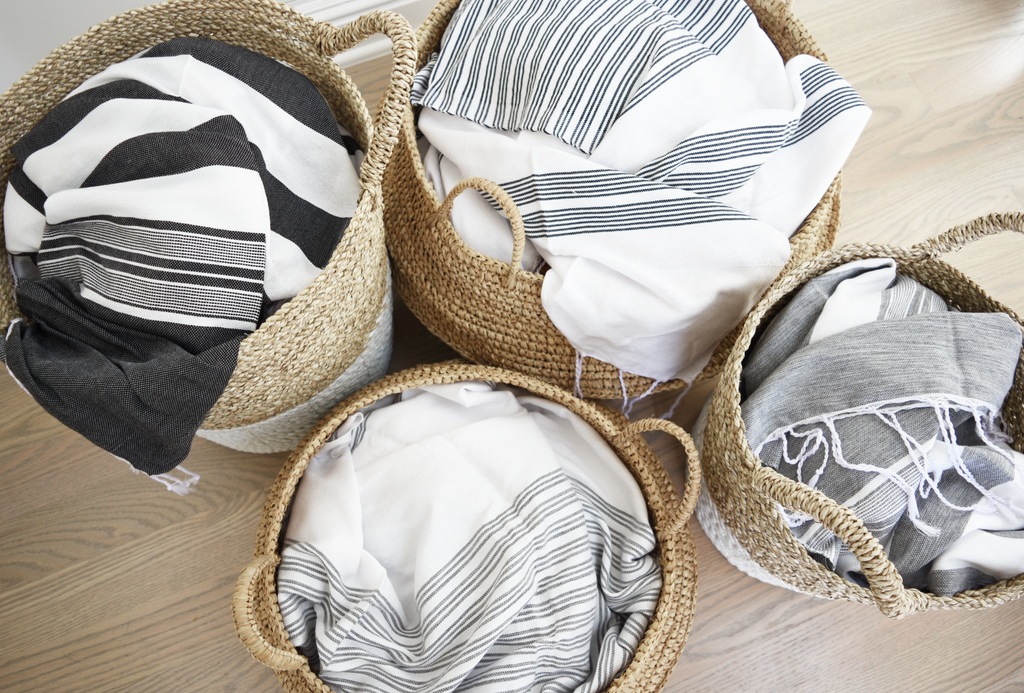 Four two-toned structured hyacinth storage baskets filled with striped textiles on wood floor