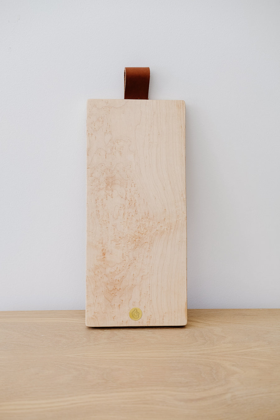 Font view of Studio Inko's Bird's Eye Maple Cutting and Serving Board against a white wall. - Saffron and Poe