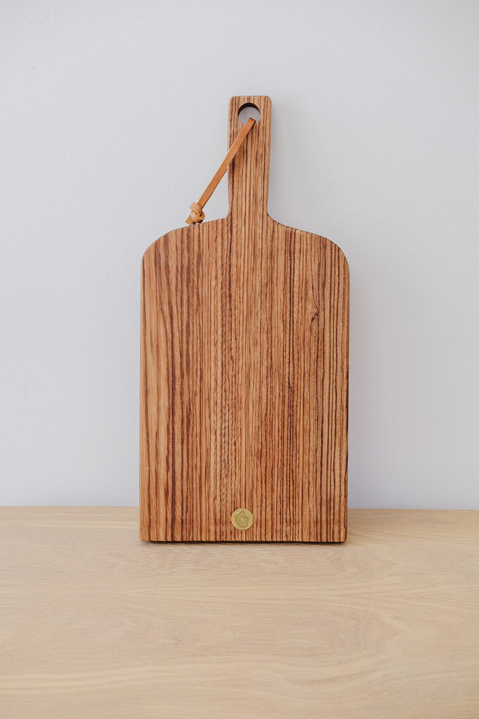 Front view of Studio Inko Zebrawood Cutting and Serving Board against a white wall. - Saffron and Poe