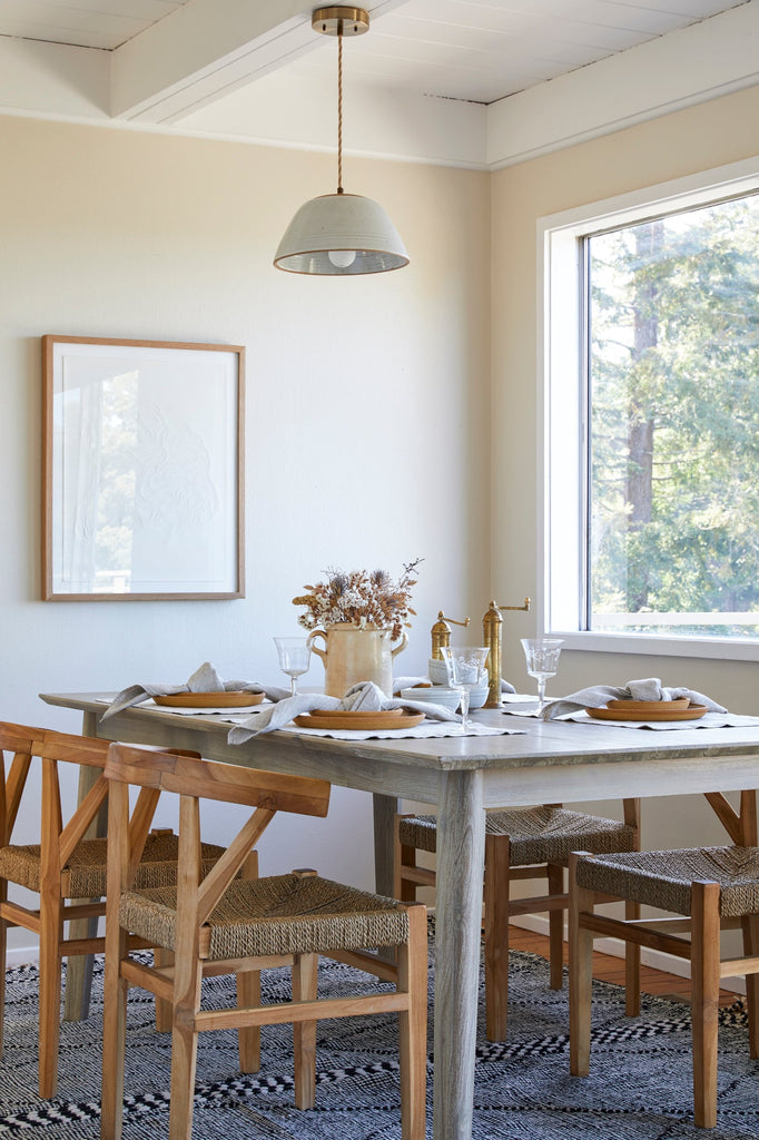 Style view of our Rattan Curved Back Dining Chairs with dining table set with our Teak Plates, Atlas Salt and Pepper Grinders, and Italian Confit Pot. Revivalist South art work, Ceramic Pendant, and Moroccan Flat Weave Kilim Rug included. - Saffron and Poe