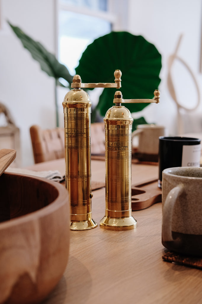 Front styled view of the brass Atlas salt and pepper grinder set on oak table with the teak salad bowl. - Saffron and Poe