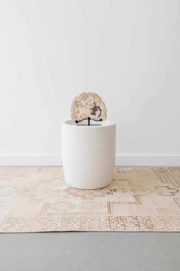 Styled view of Abalone Terrazzo Side Table on a Vintage Turkish Oushak Rug with a Petrified Wood Sculpture against a white wall. - Saffron and Poe