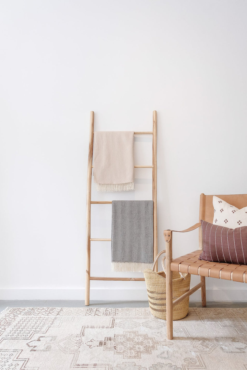 Beige baby alpaca throw blanket hanging on wooden ladder in minimalist living room setting with neutral decor and woven basket