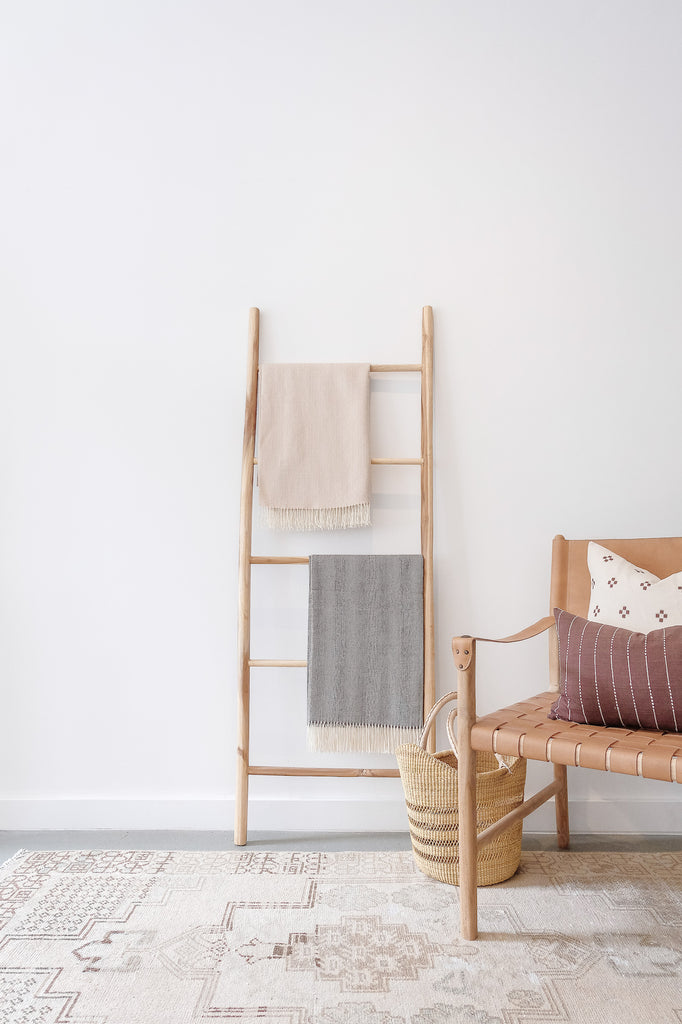 Styled Alpaca Throw Blankets on a teak wood blanket ladder next to a Leather Strap Safari Chair. - Saffron and Poe