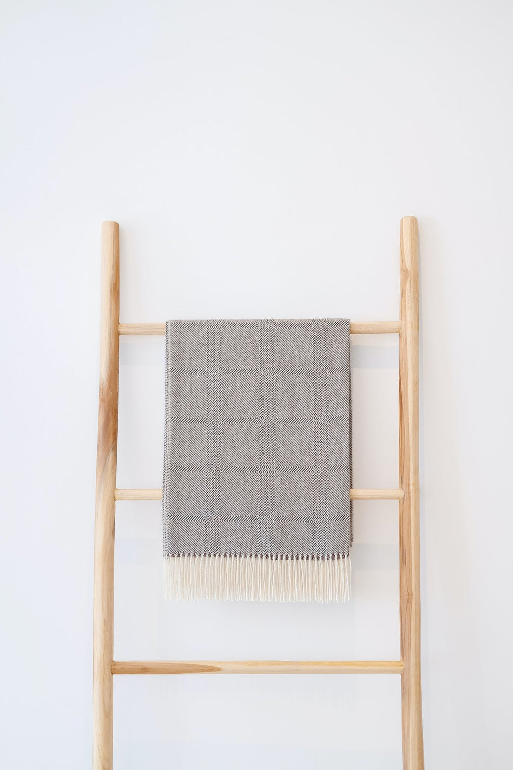 Charcoal brown baby alpaca throw blanket with geometric pattern and fringe on wooden ladder against white wall