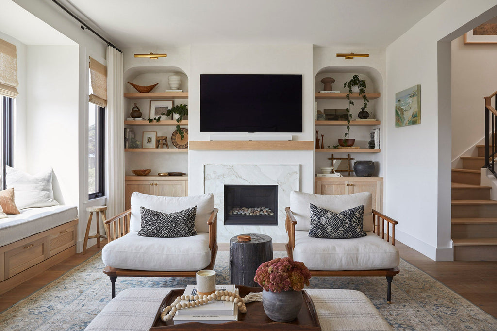 Antique Miao lumbar pillows on modern white armchairs in cozy living room with fireplace and wooden shelves