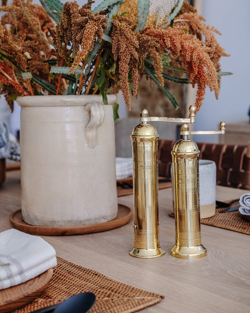 Styled Brass salt and pepper Grinders on an Oak Dining Table next to an Italian Confit Pot with flowers