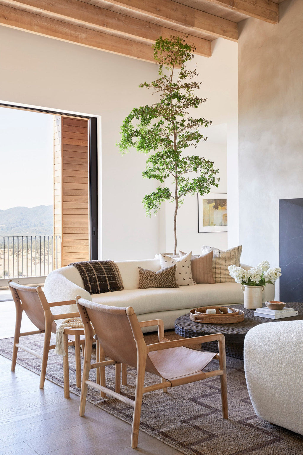 Beige embroidered pillow on a modern sofa in a sunlit living room with wooden chairs and green plant