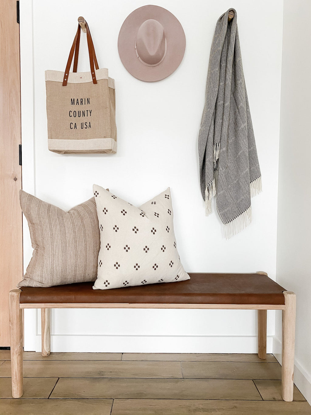 Beige embroidered pillow with neutral patterns on a wooden bench in a minimalist room setting