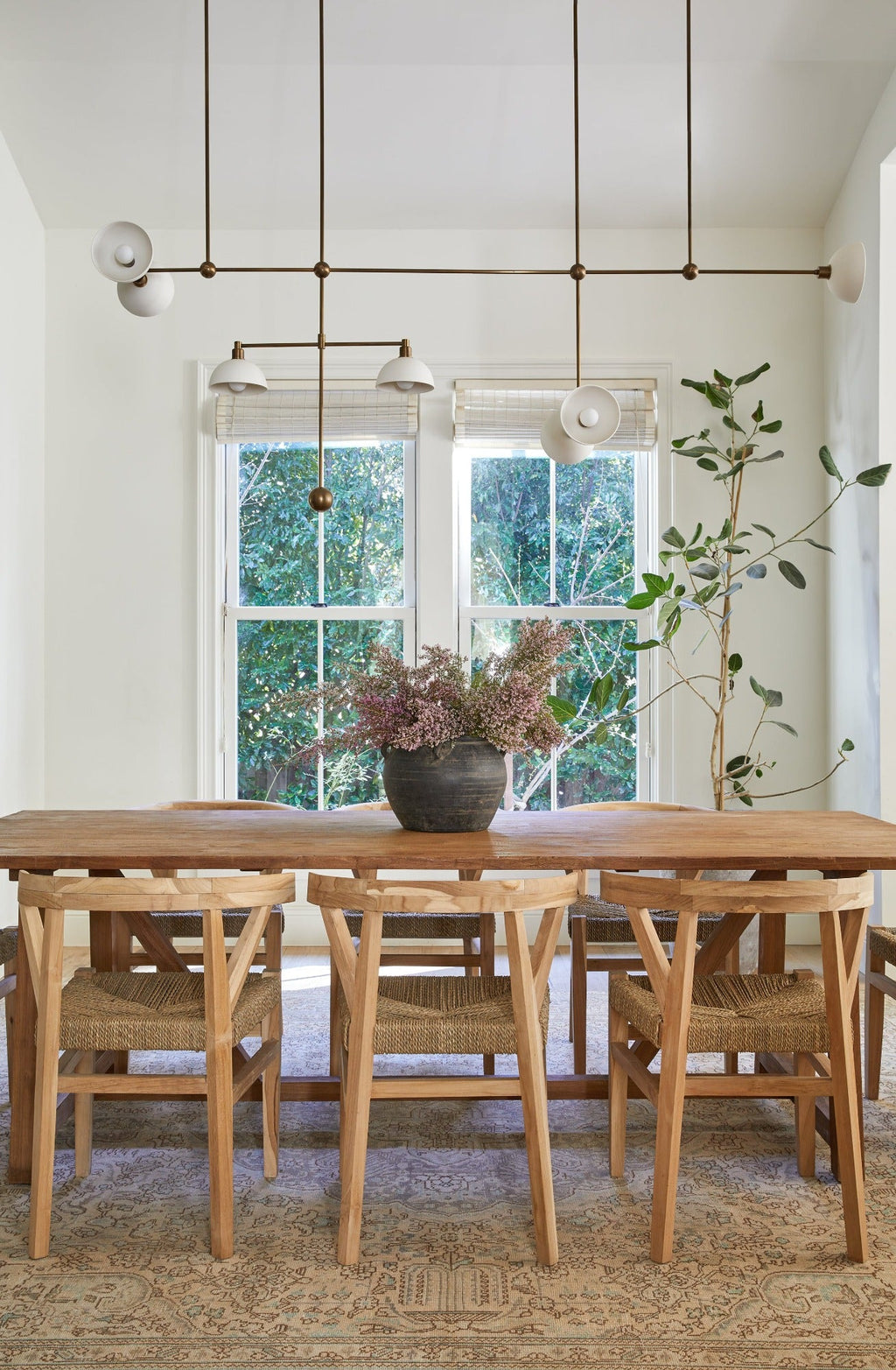 Woven Wishbone dining chairs with braided rattan seats and teak frames around wooden table in bright dining room