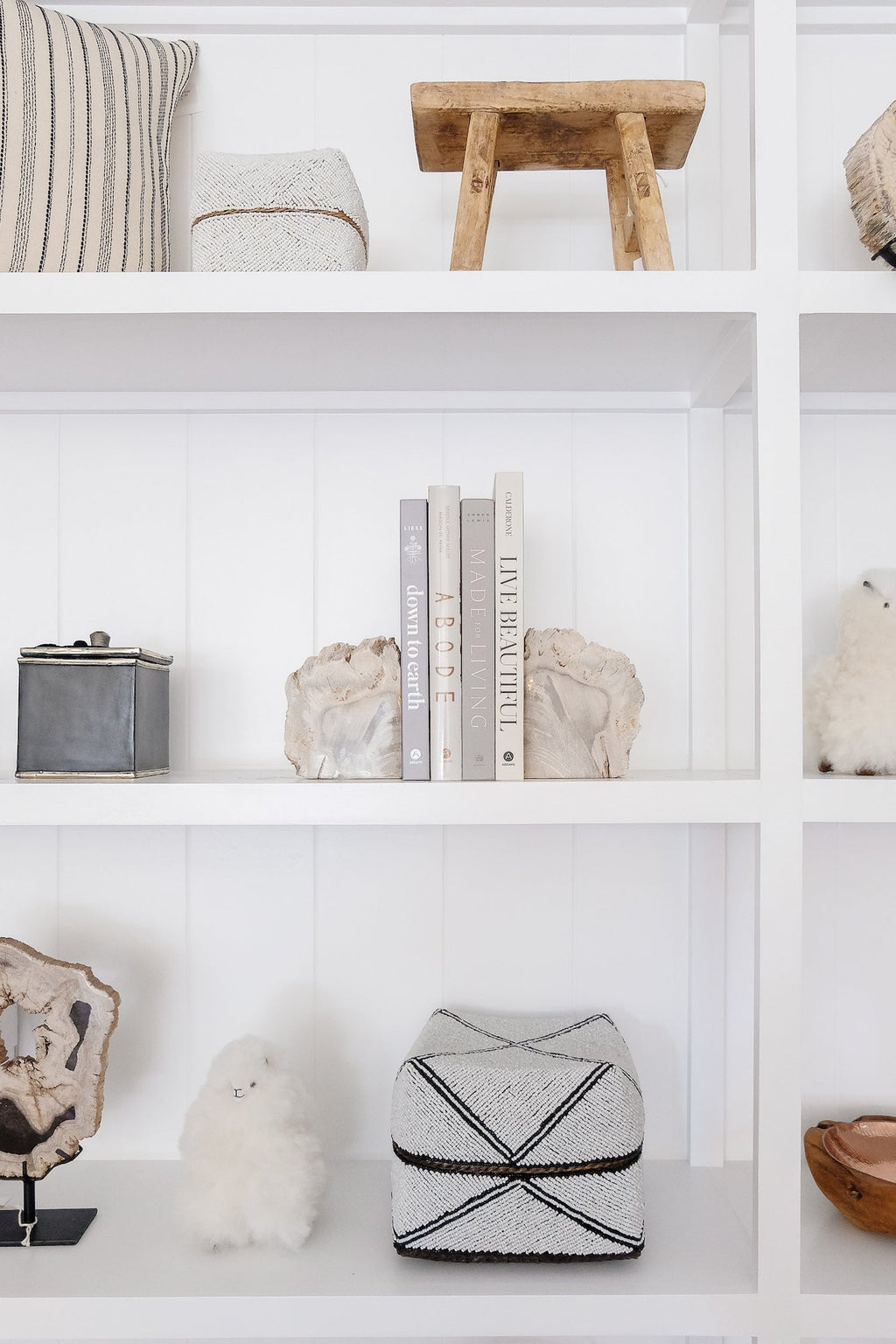 Minimalist white shelving with rustic wooden stool, neutral decor, natural stone bookends, and handcrafted objects in a serene Abode interior.